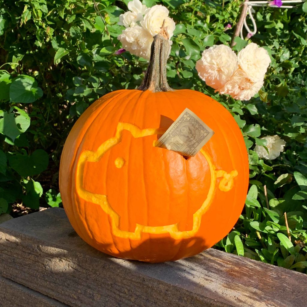 Piggy bank carved into pumpkin with cash sticking out of the slot