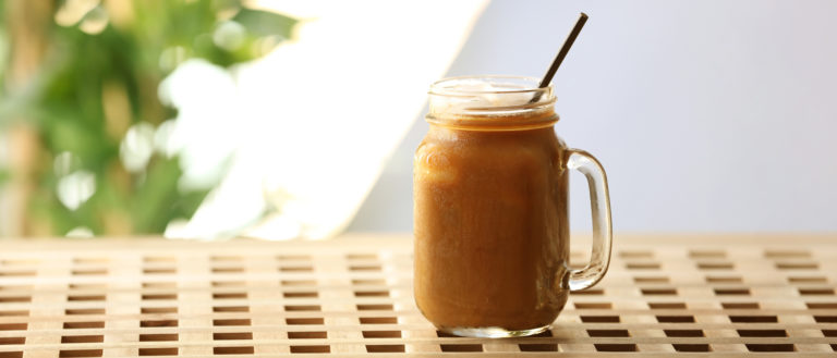 Iced coffee in a mason jar with a straw on a wooden surface.