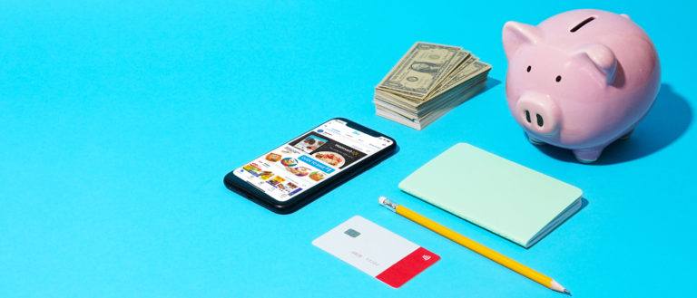 A phone, stack of cash, piggy bank, and notepad on a blue background