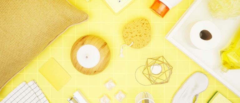 various dorm-related items laid out on a yellow backround: pillow, humidifier, toilet paper, laundry detergent, loofah, sleeping mask