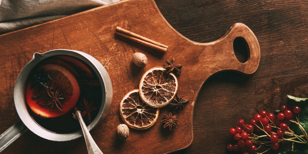 A cup of mulled wine on a wooden cutting board surrounded by aesthetically arranged dried fruit and spices.